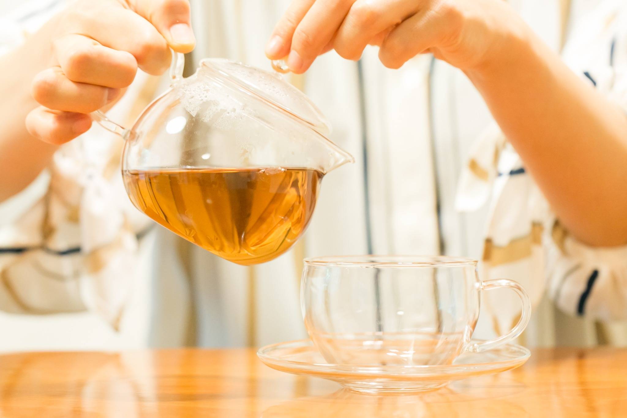 ガラスのティーポットからハーブティーをカップに注いでいる手元の様子